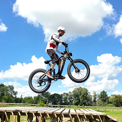 A cyclist on a golden e-bike jumping off a wooden ramp, with blue sky and clouds in the background